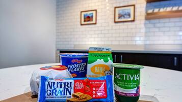 A kitchen counter with various food items including a bag of Nutri-Grain breakfast bars, a carton of milk, a container of frozen flakes, and a container of Activia yogurt.