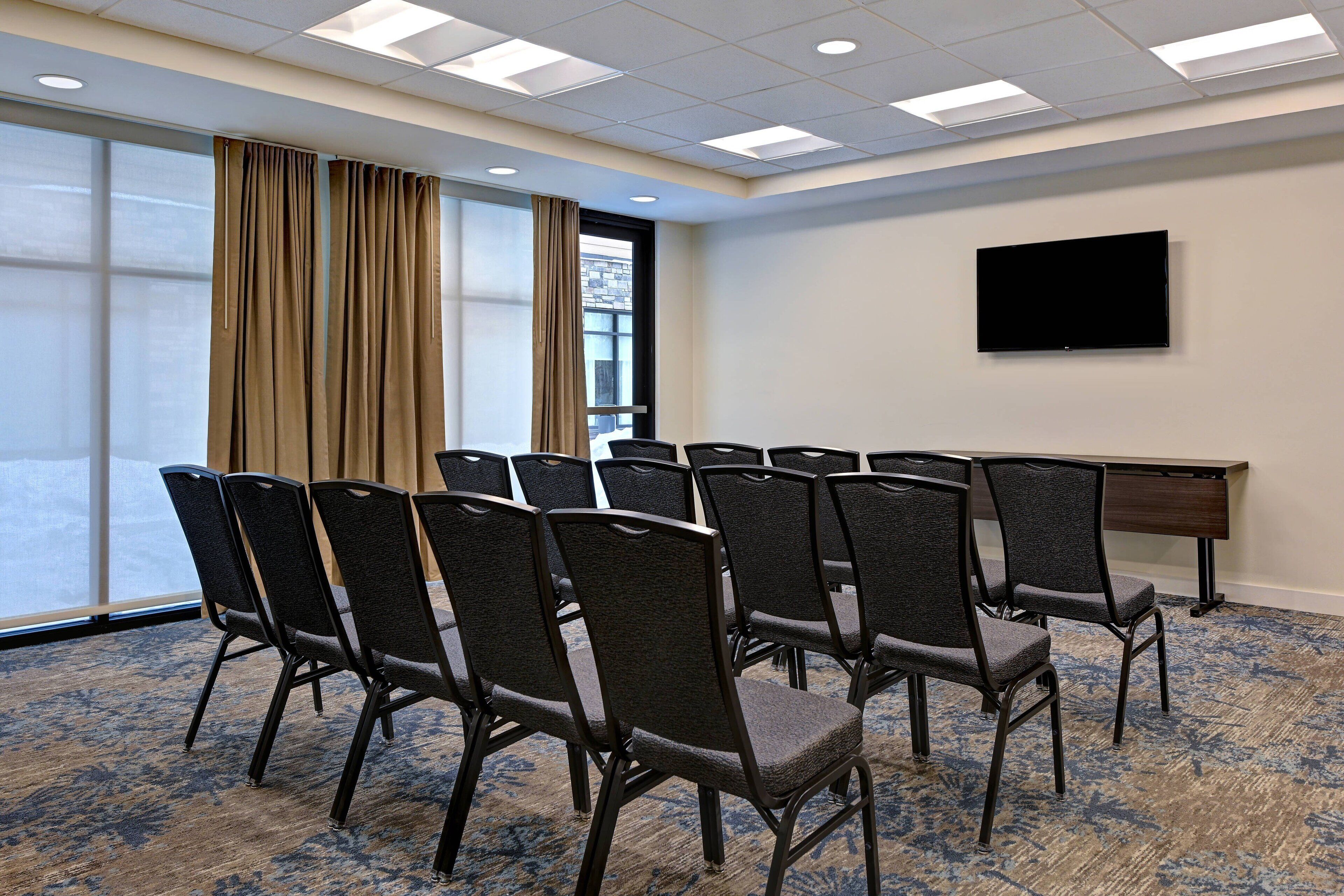 A conference room with a large window, a flat-screen TV, and a carpeted floor.
