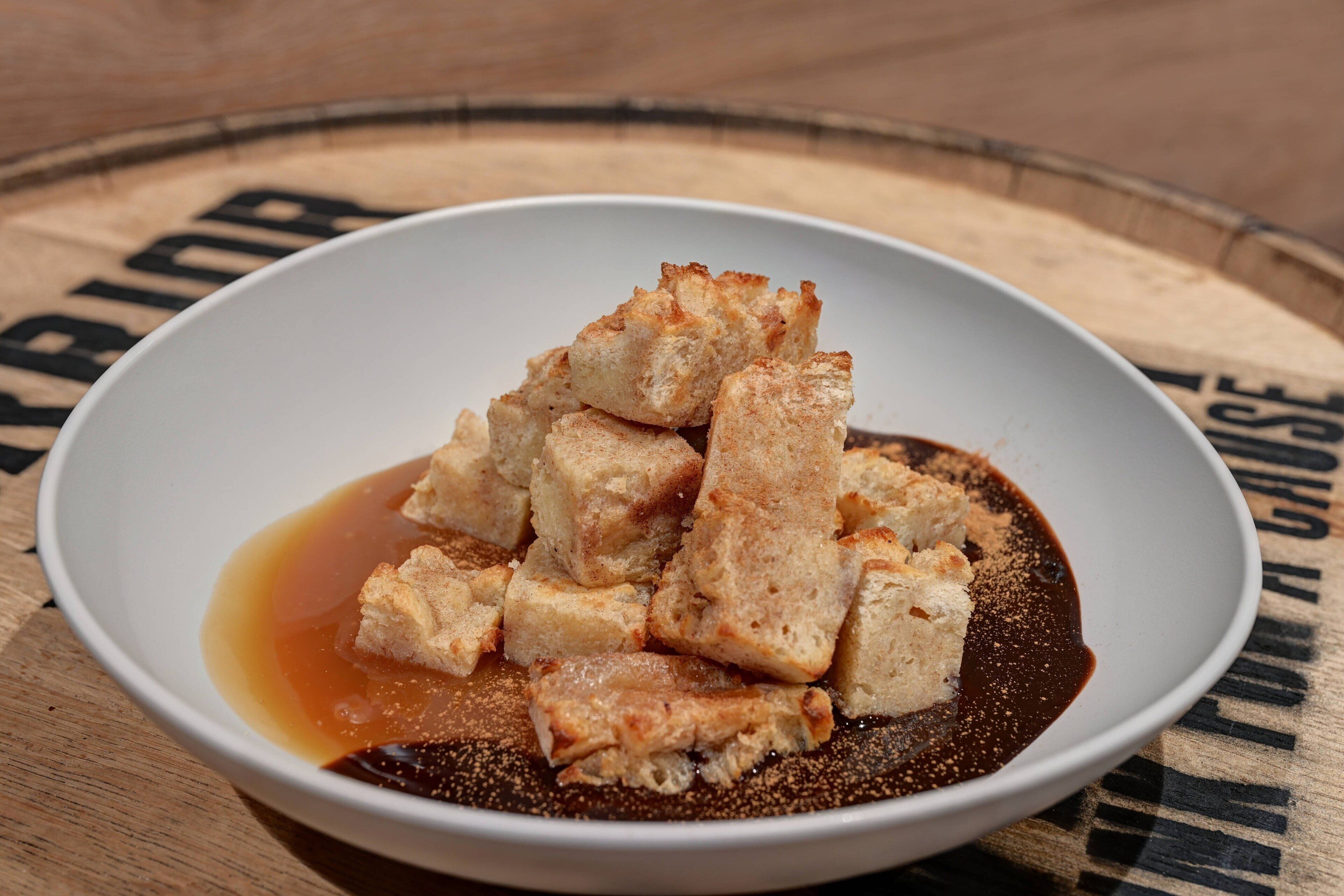 A bowl of food with cubes and a liquid sauce on a wooden surface.