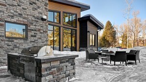 A modern outdoor kitchen area with a stone barbecue, outdoor seating, and a view of a residential building. - Residence Inn by Marriott Steamboat Springs (Steamboat Springs)