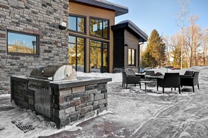 Un área de cocina exterior moderna con una parrilla de piedra, asientos al aire libre y vistas de un edificio residencial.