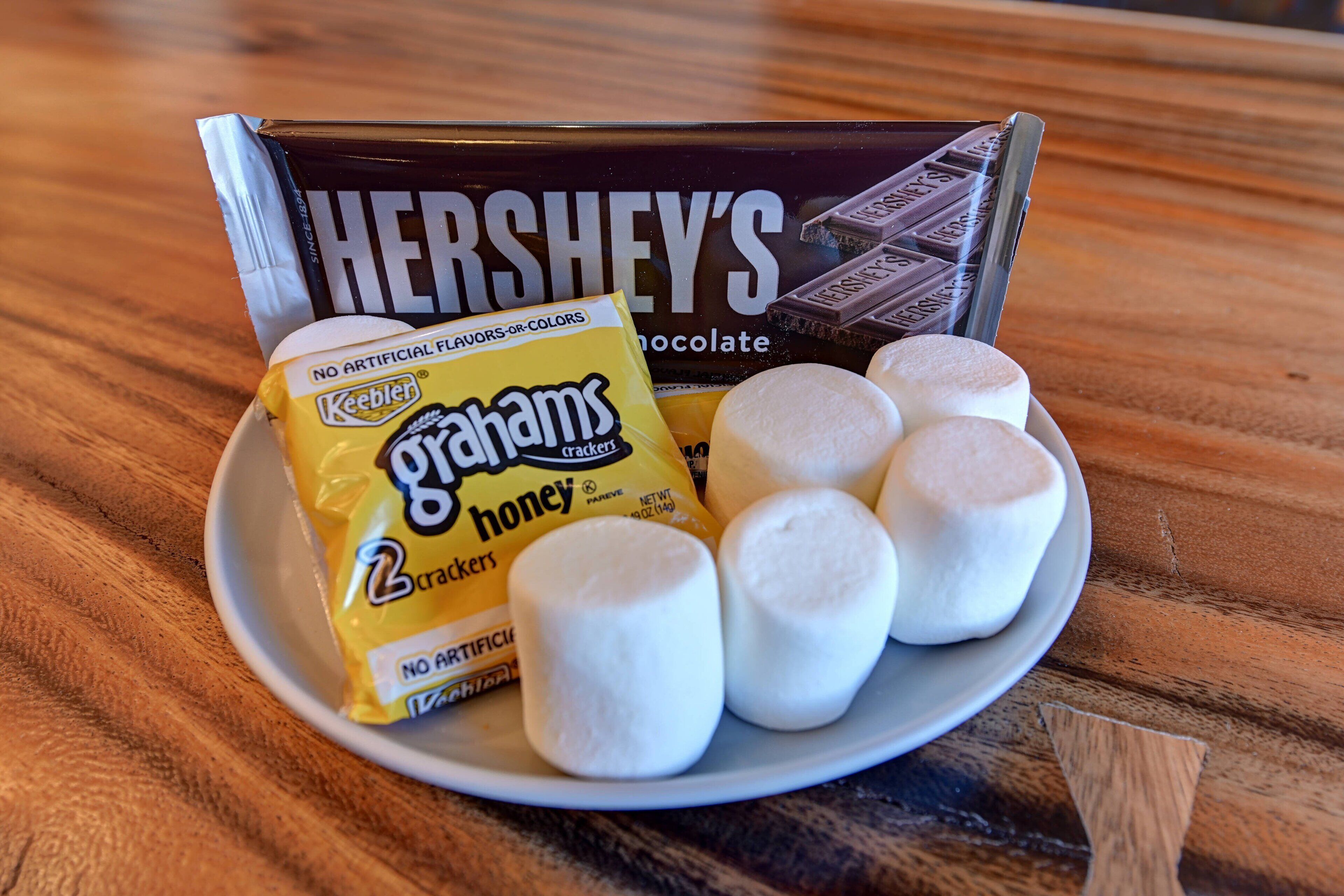 A plate with marshmallows, a pack of Ghirayams crackers, and a Hershey's chocolate bar.