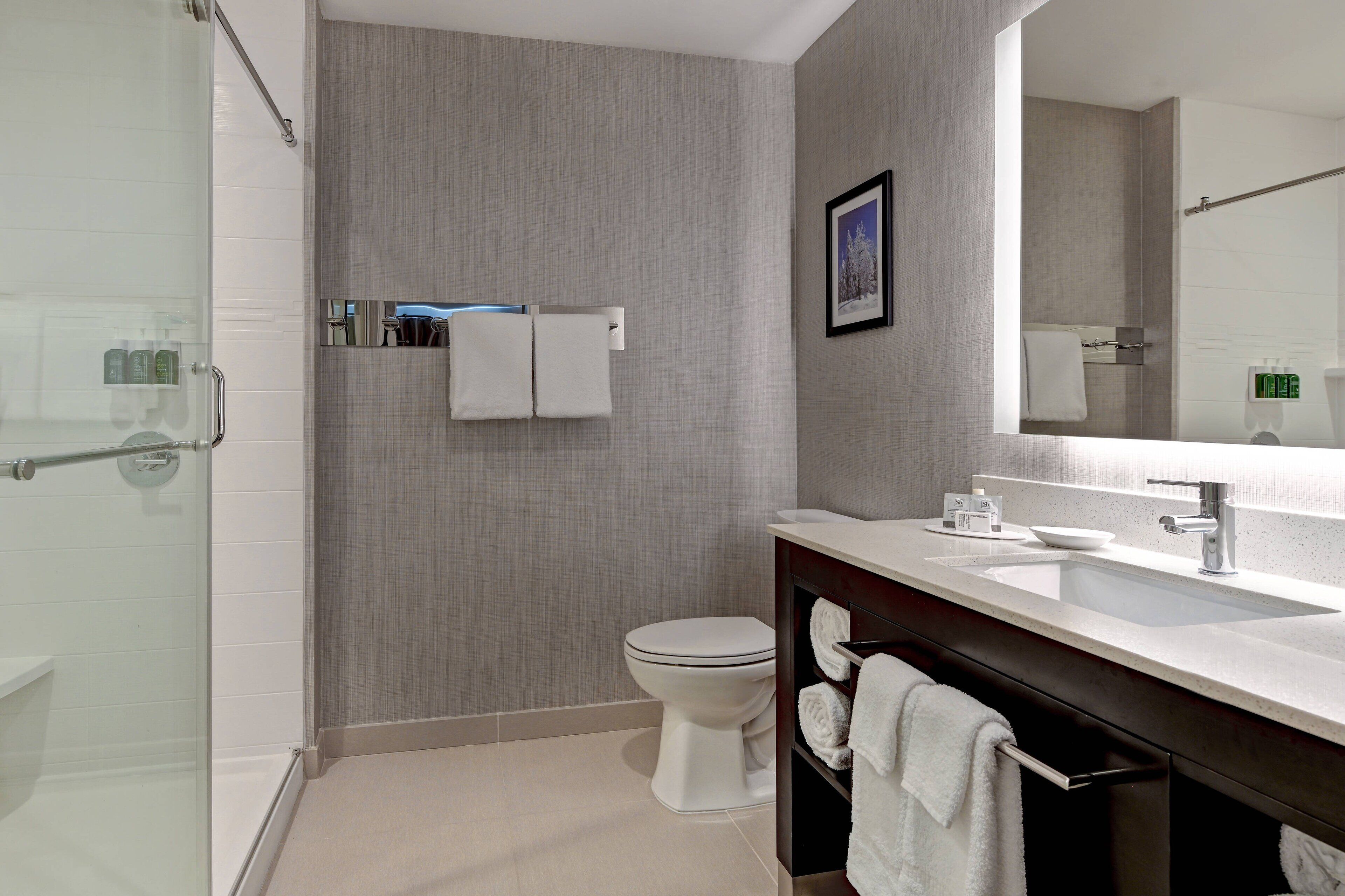 Une salle de bain moderne avec une douche à parois de verre, des toilettes blanches, un meuble-lavabo et un porte-serviettes.