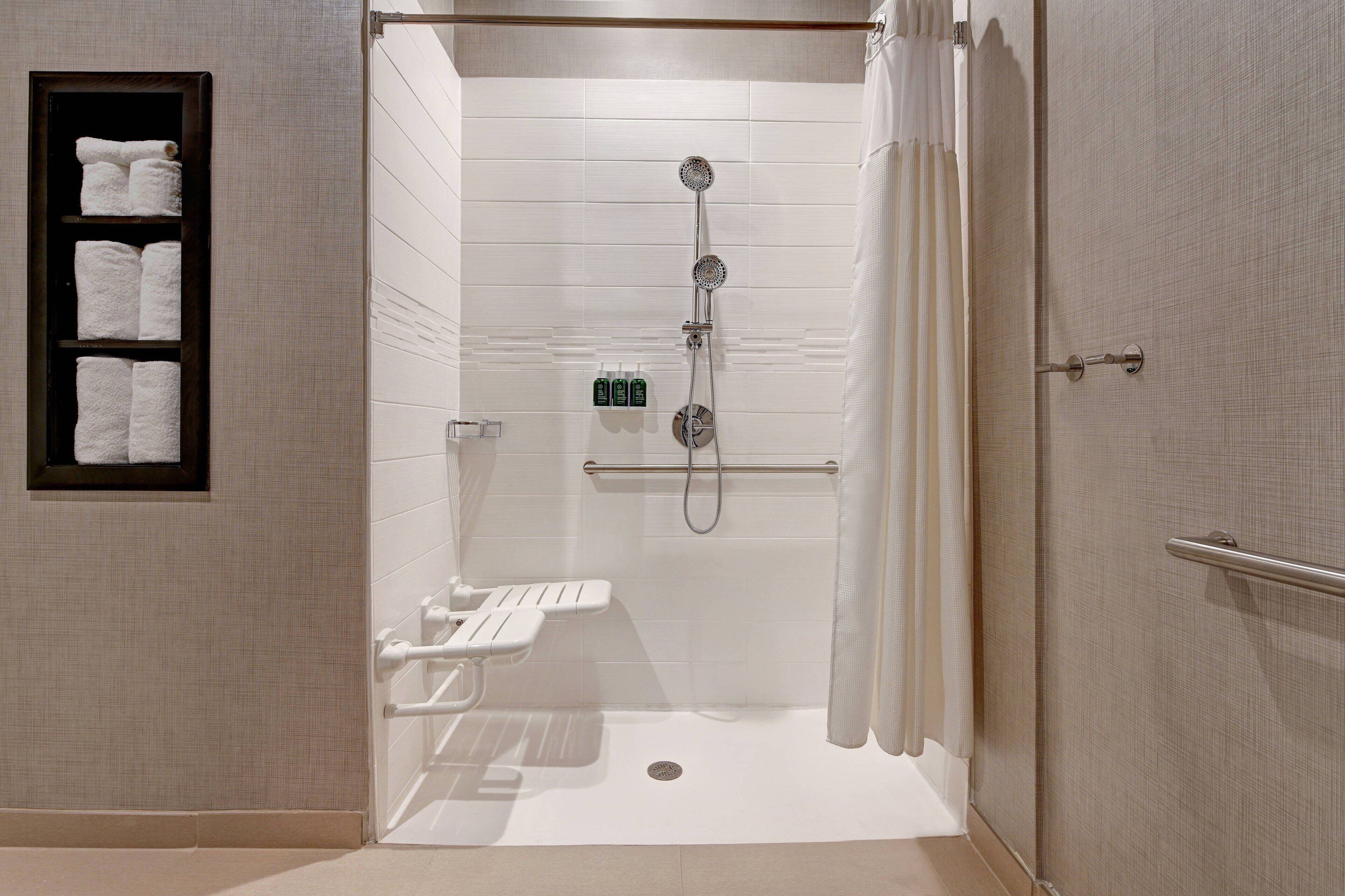 A walk-in shower with a glass door, a towel rack with folded towels, and a handheld showerhead.