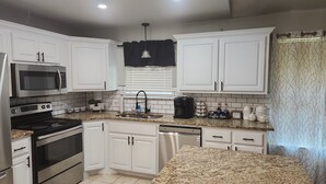 A modern kitchen with white cabinetry, stainless steel appliances, a granite countertop, and a coffee station. - Beautiful Lake Front home w/ sunroom and outdoor patio, (Stigler)