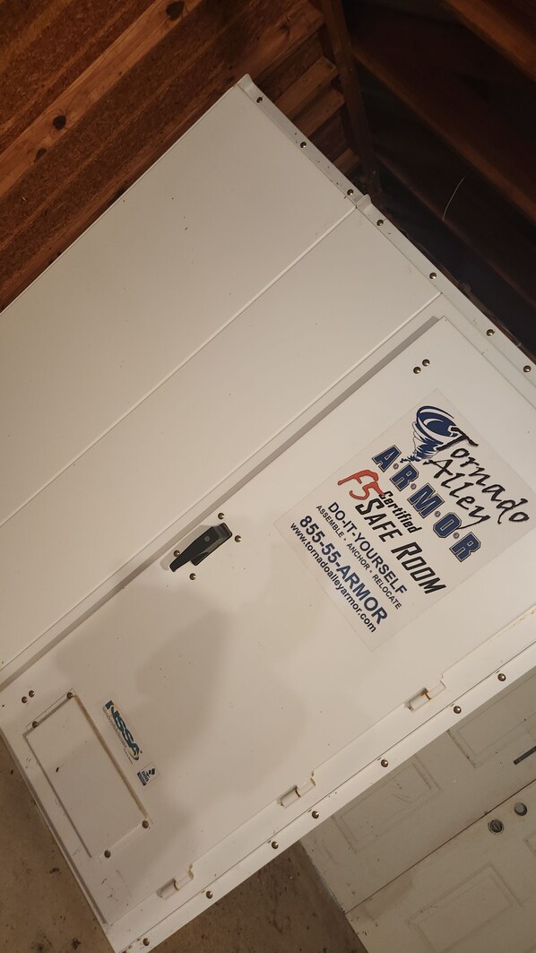 A white storage box with a label for Tornado Safety Room, including a certification logo and contact information.