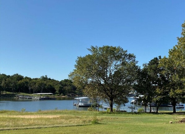 A serene lakeside view with a grassy area, a covered pavilion, and a dock with boats.