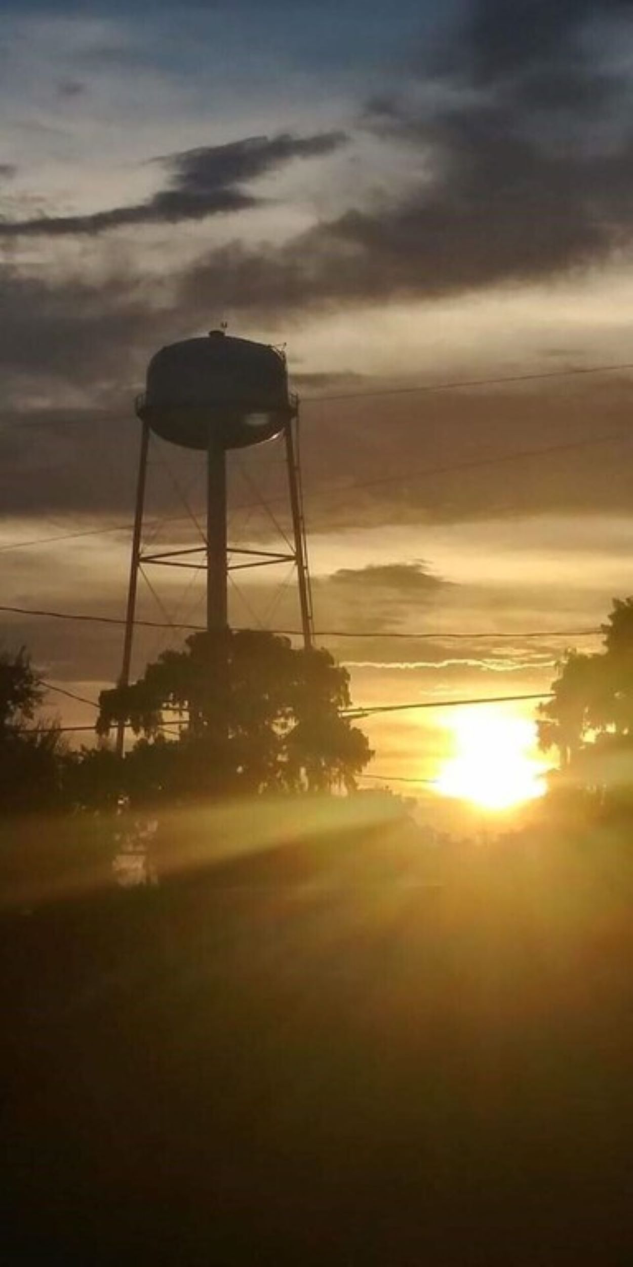 A water tower silhouetted against a sunset with a clear sky.