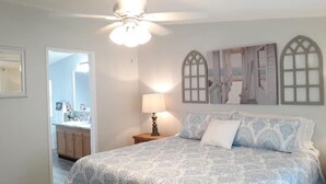 Quarto com uma cama, mesa de cabeceira, luminária e ventilador de teto.