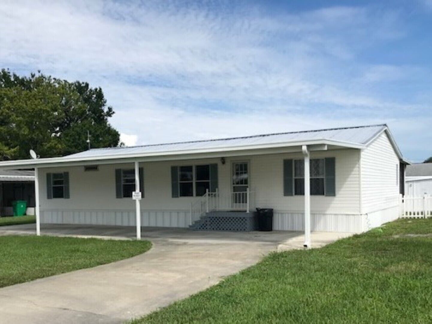 A single-story white building with a covered porch, a small front entrance, and a trash can.