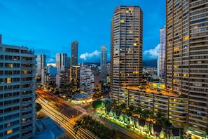 A high-rise hotel with multiple floors, a rooftop pool, and a well-lit urban street below. - Amazing Ocean View, Prime Waikiki Location! Minutes to beach, Parking + Washer/Dryer! (Honolulu)