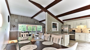 Een ruime eethoek met een donker houten tafel, witte stoelen en geweven placemats.