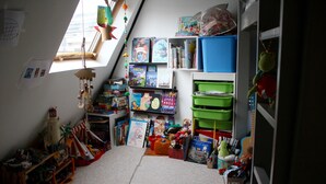 Un cuarto infantil con una cama elevada, estantes con libros y juguetes, y una ventana con vista al exterior.