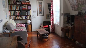 Una sala de estar acogedora con un sofá, una mesa de centro, una estantería y una ventana con cortinas.