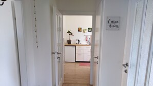 A hallway leading to a kitchen with white cabinets, a potted plant, and a Buddha statue.