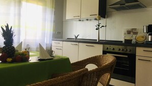 A kitchen with white cabinets, a stove, and a sink. There is a wicker chair and a table with a green tablecloth.