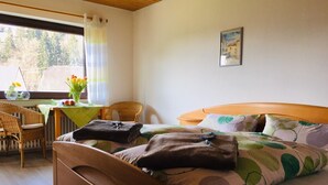 A bedroom with a wooden bed, a table with a green tablecloth, wicker chairs, and a window with curtains.