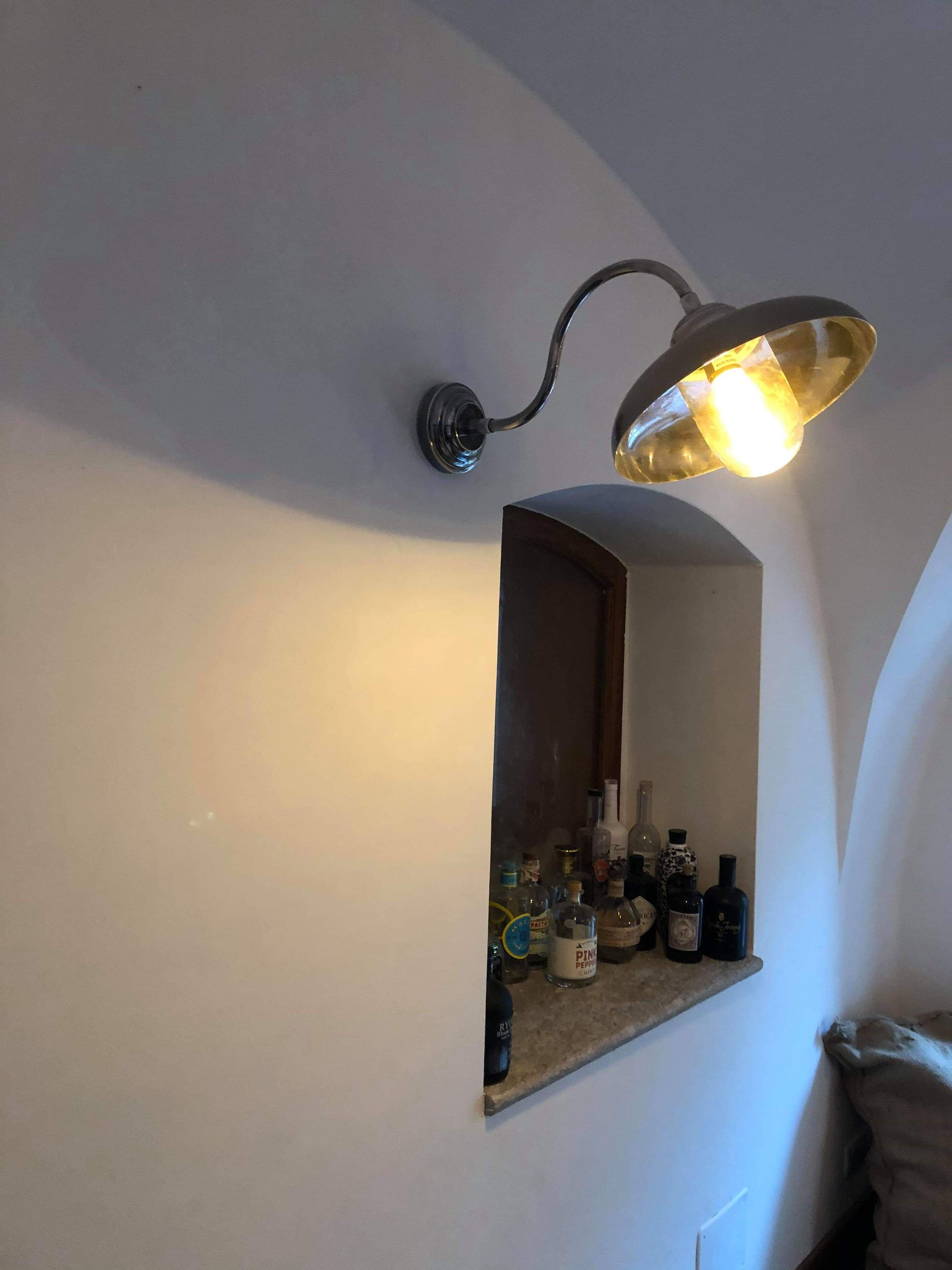 Een wandplank met verschillende flessen, een spiegel en een wandlamp.