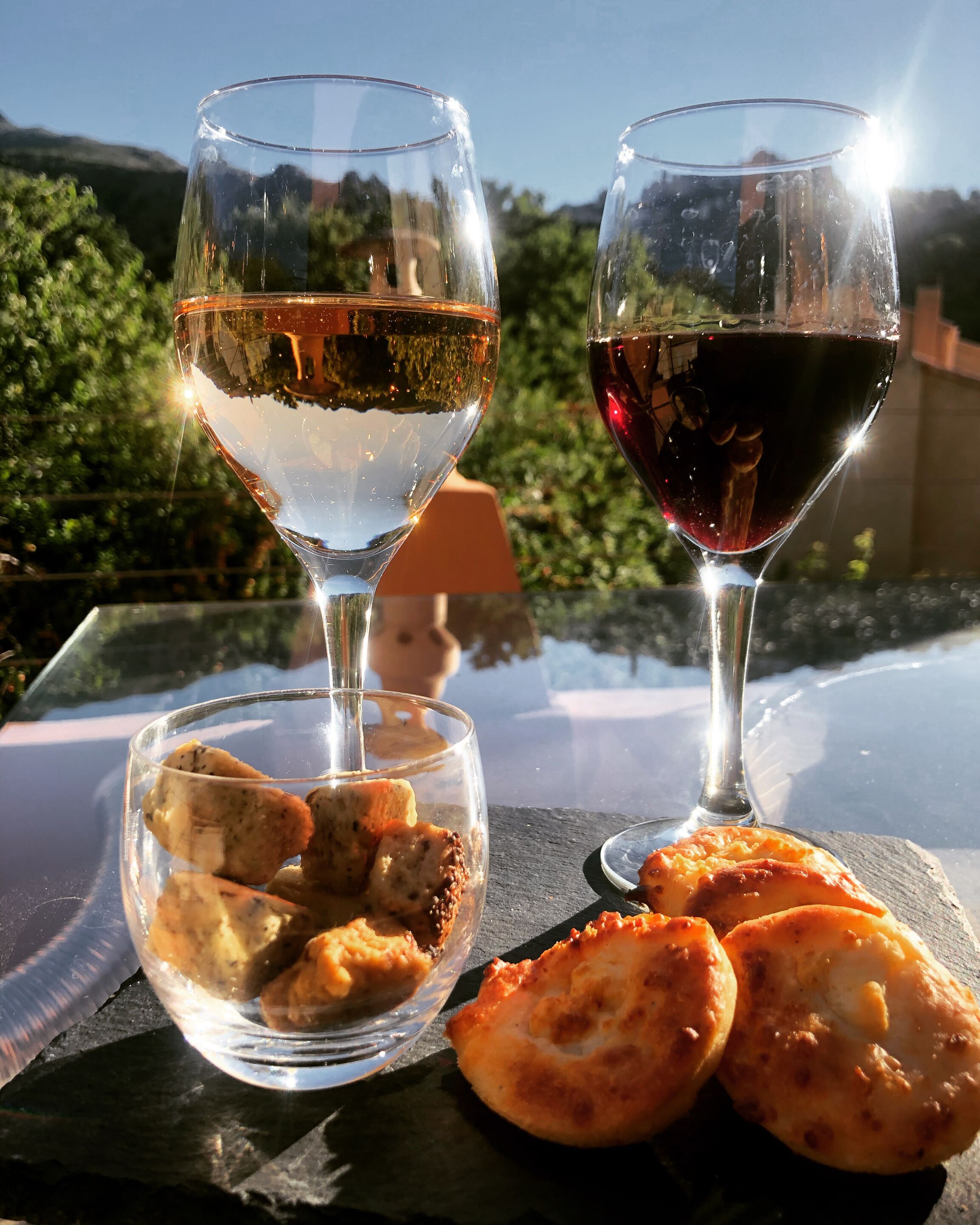 Two glasses of wine and a bowl of food on a table outdoors.