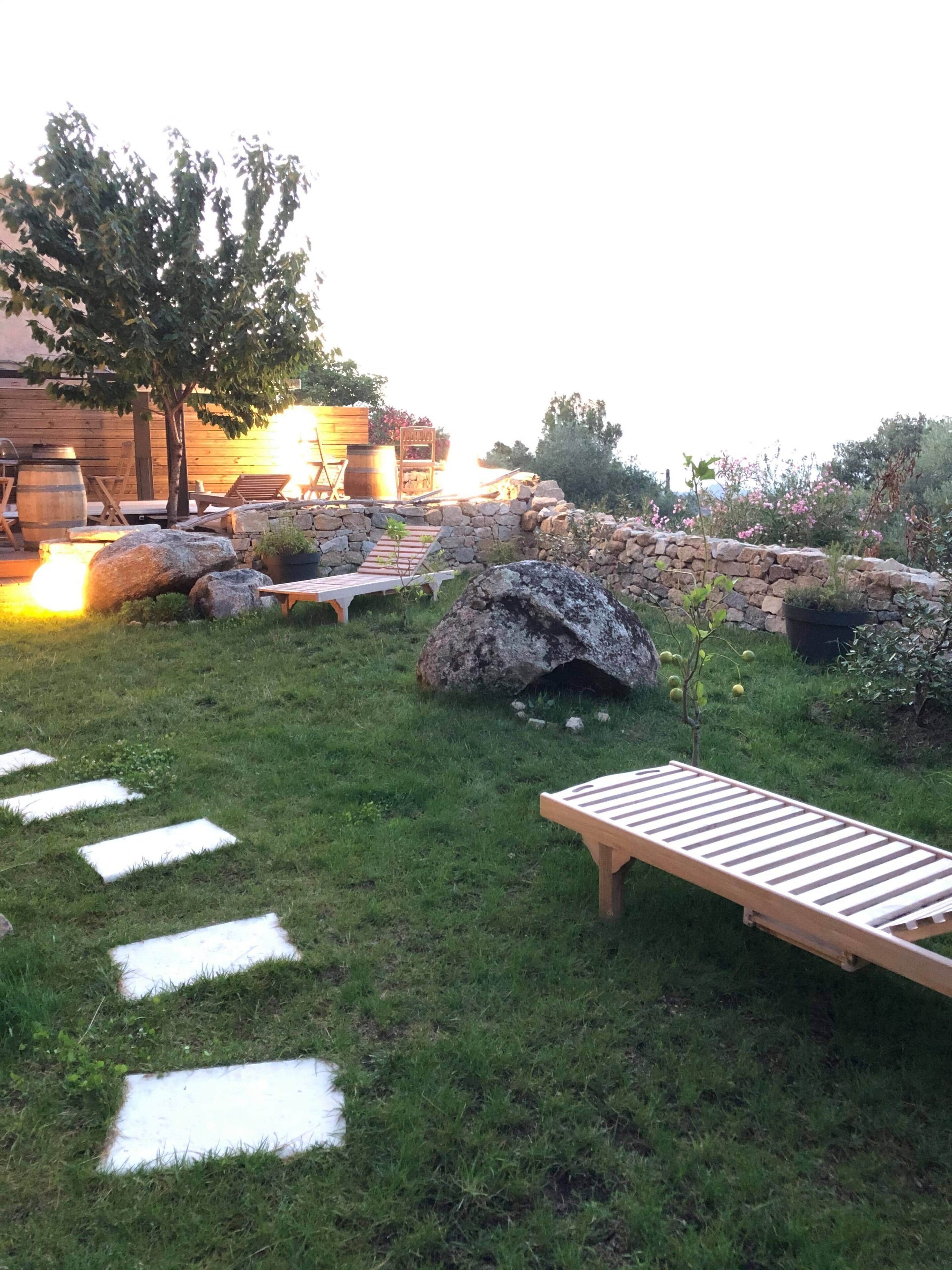 A garden with a wooden deck, stone walls, and a rustic outdoor seating area.