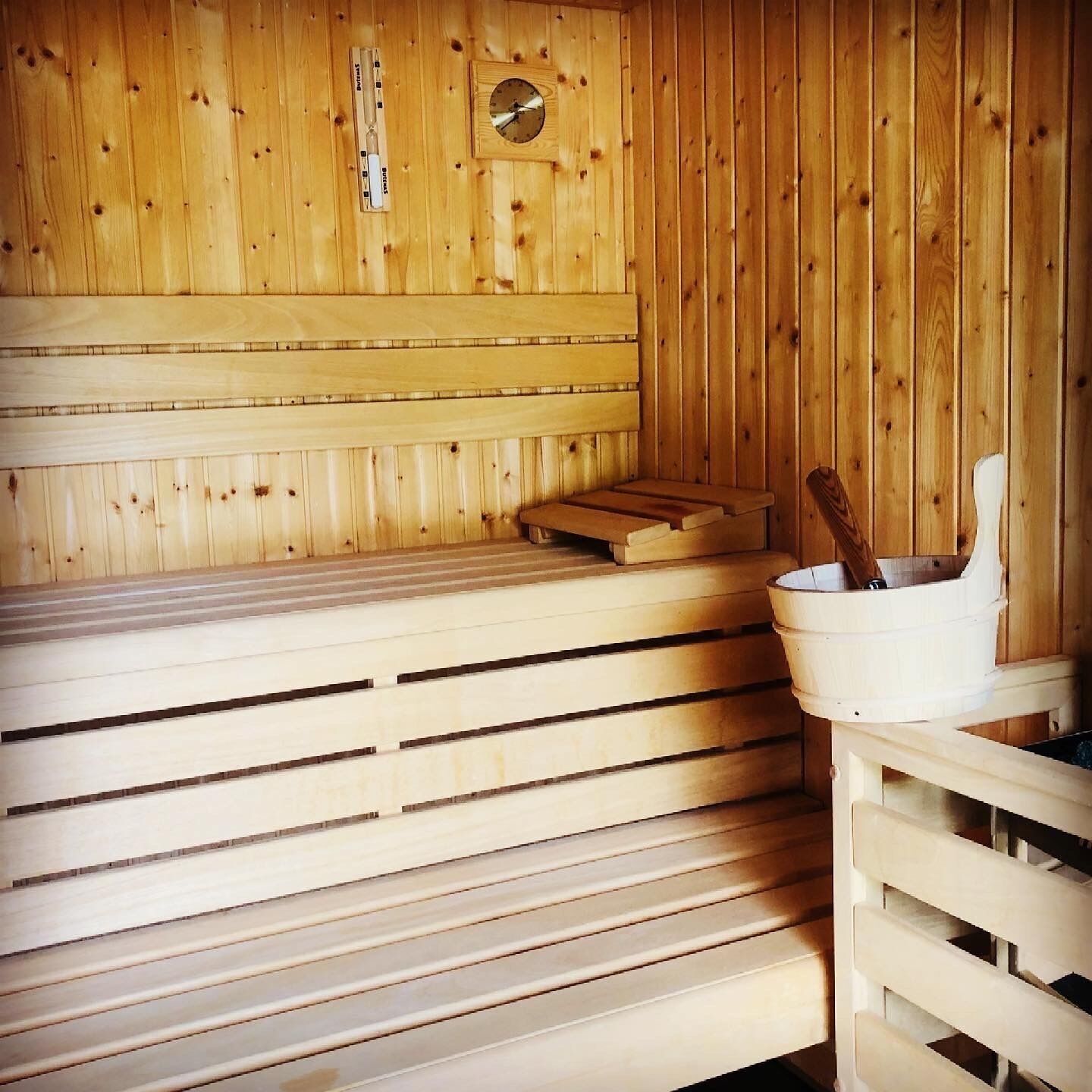 A wooden sauna room with benches, a wooden bench, and a bucket with a wooden mallet.
