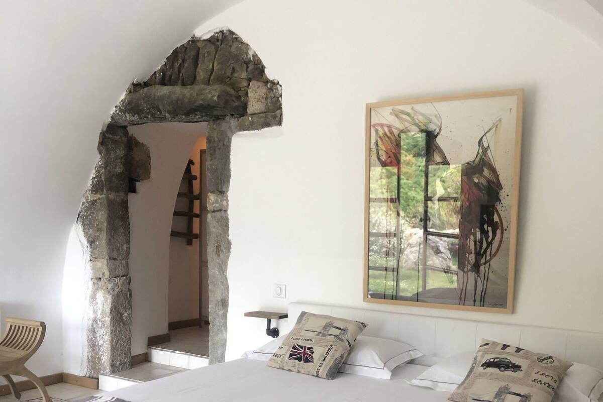 Un dormitorio con una cama grande, un arco de piedra, un cuadro y vistas a un jardín.