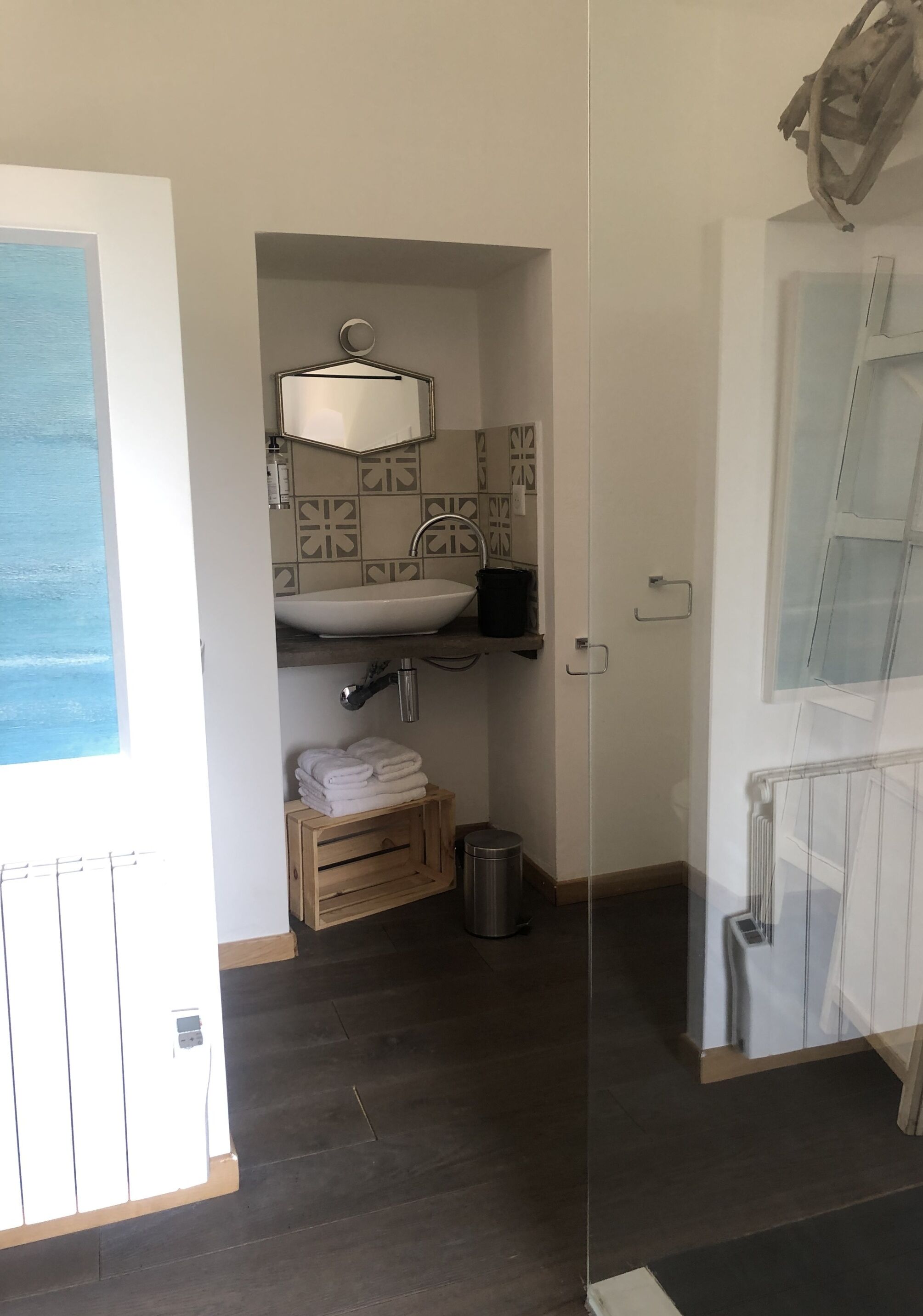 Een badkamer met een wit wastafel, een spiegel en een handdoekrek. Er is een raam met uitzicht op zee.