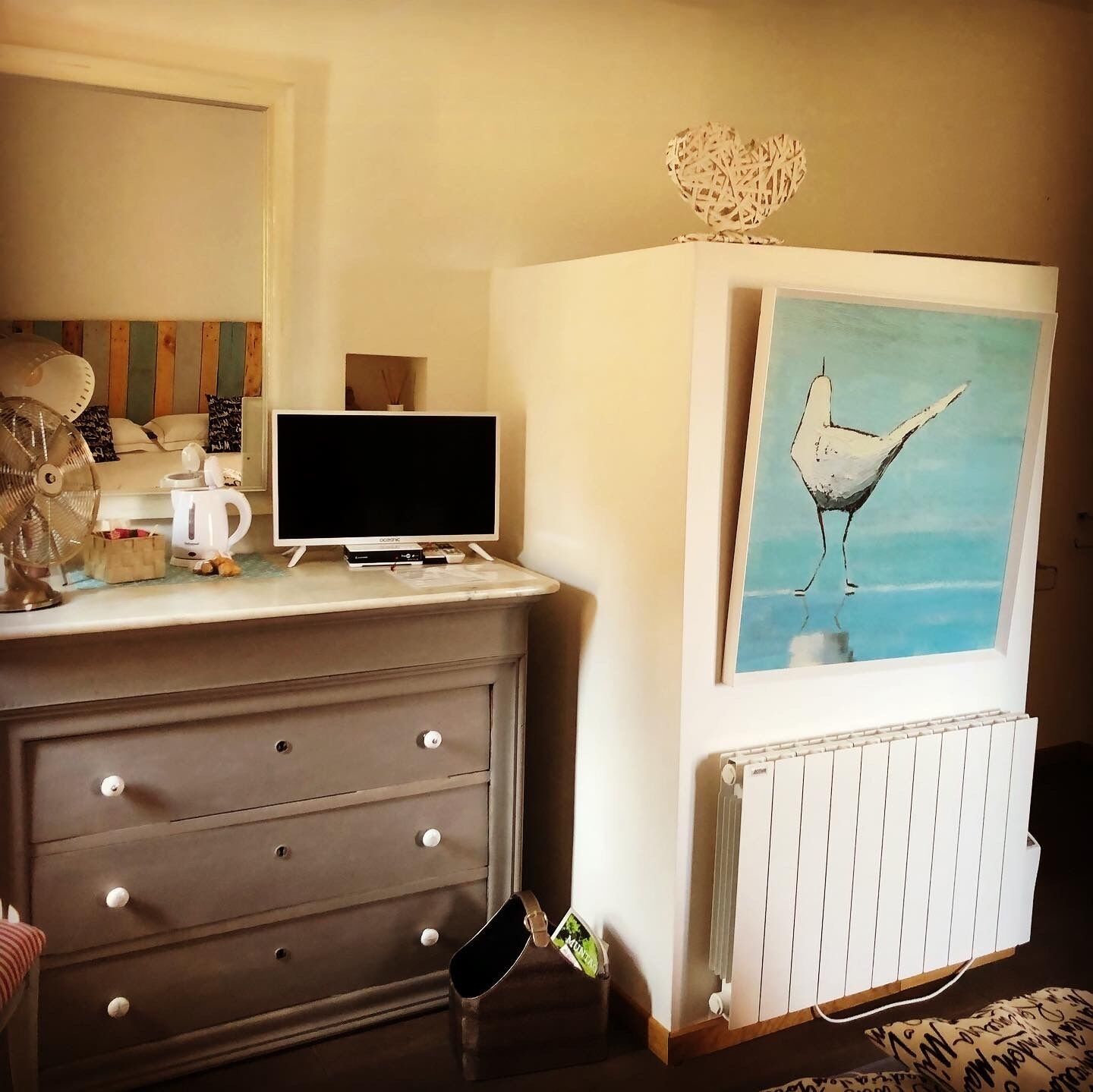 Een slaapkamer met een bed, een kapstok, een televisie en een schilderij van een vogel.