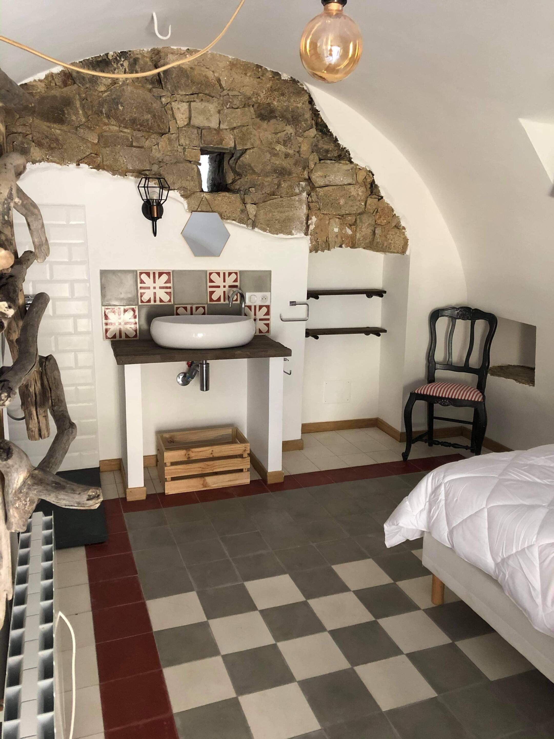 A bedroom with a stone wall, a white sink, a wooden chair, and a checkered floor.