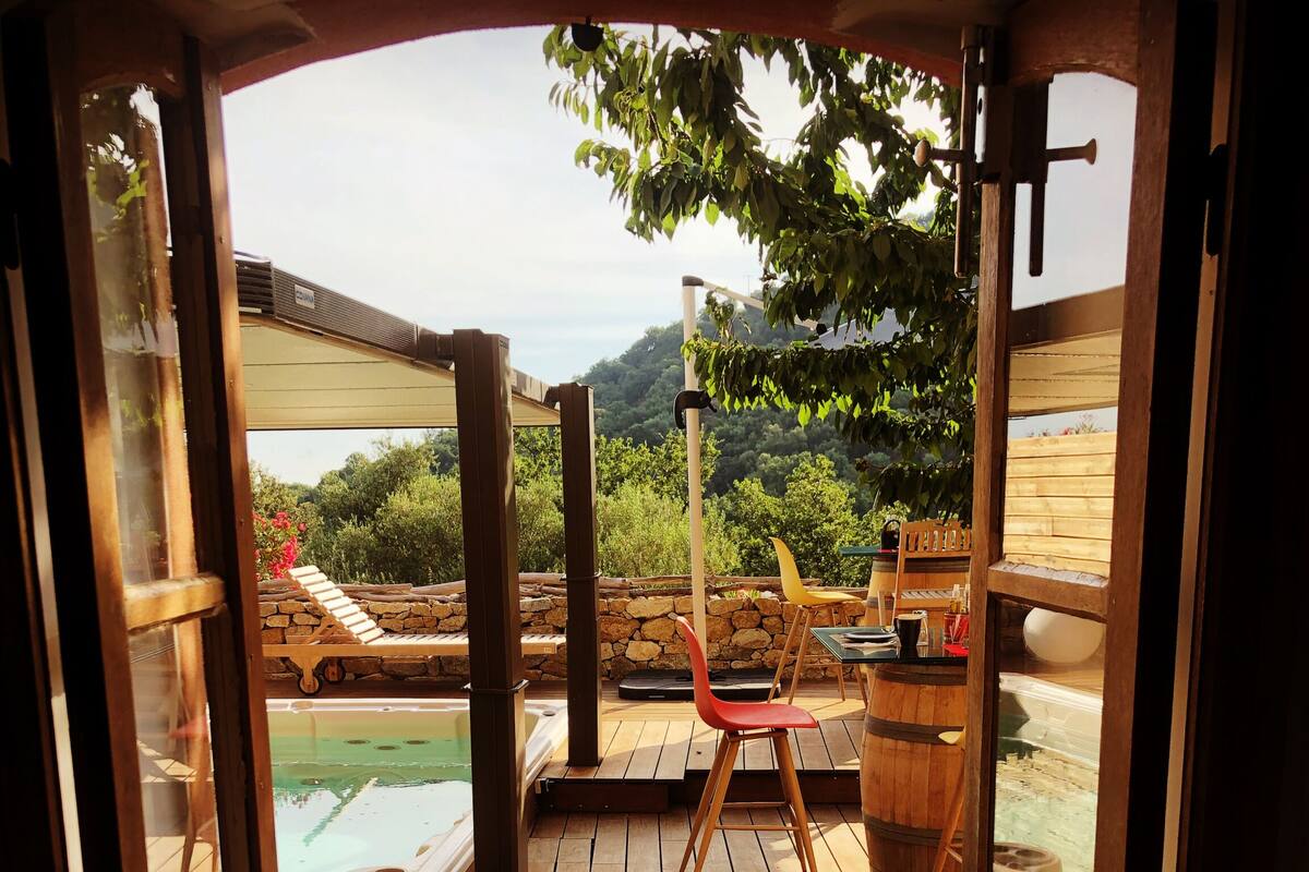 Terraza de madera con jacuzzi, sillones de descanso y pared de piedra.