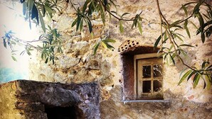 Un edificio de piedra rústico con una ventana pequeña y una maceta de barro grande.
