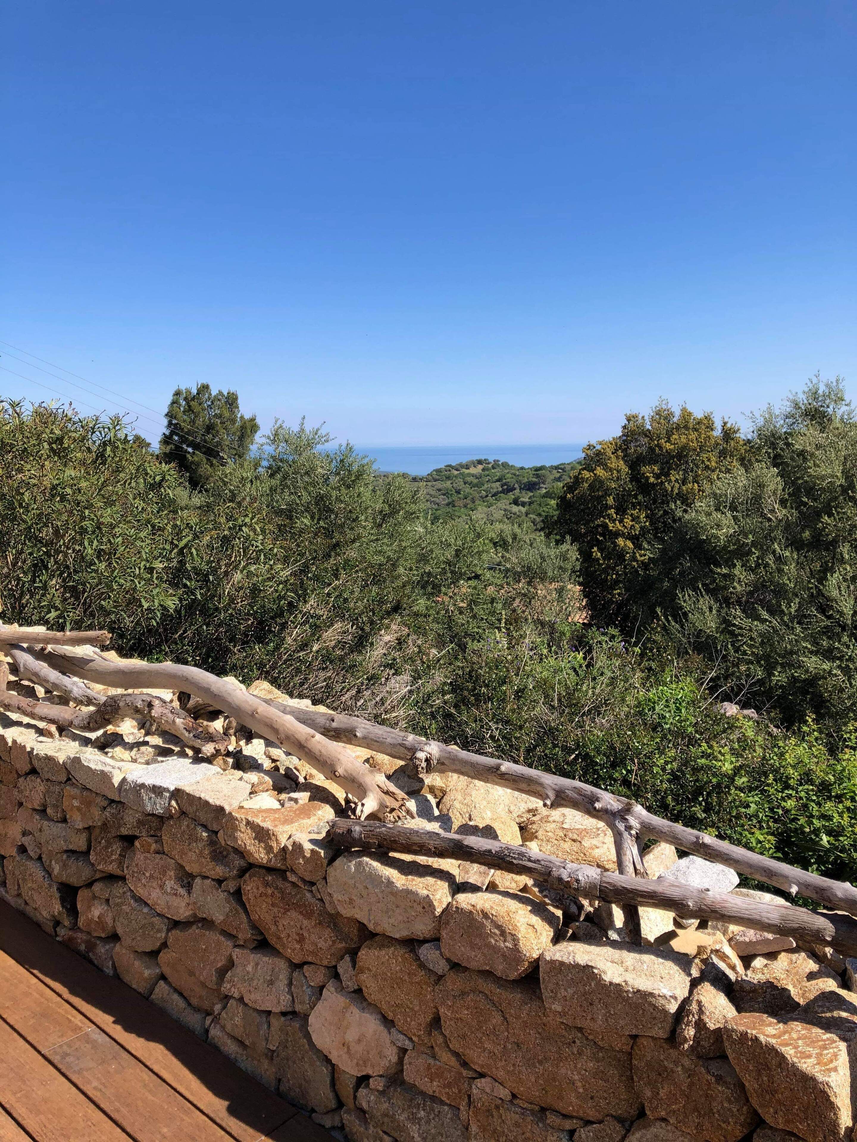 A stone wall with a wooden railing overlooking a mountainous landscape with a clear sky.