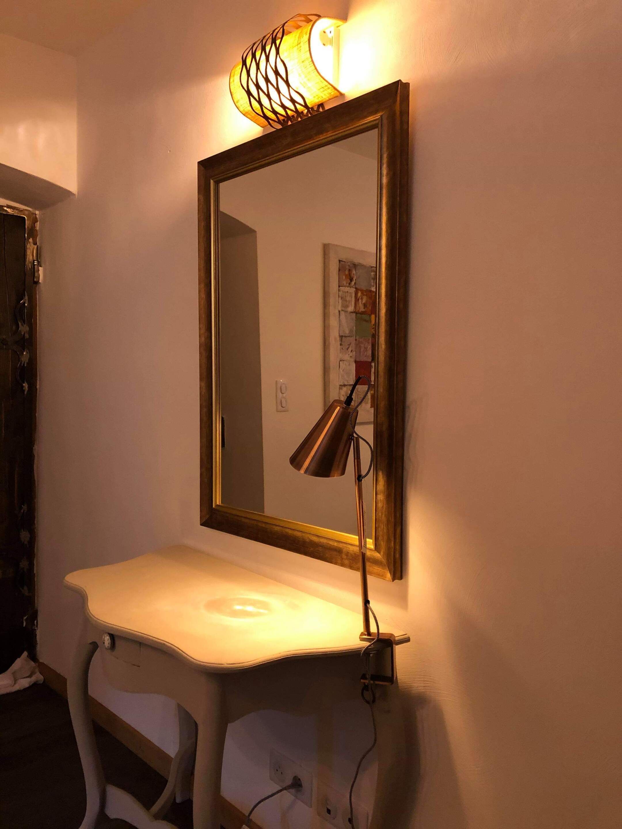 Ein Spiegel mit einer Lampe auf einem weißen Schreibtisch an einer Wand.