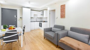Un salon moderne avec un canapé gris, une table à manger avec des chaises, et une cuisine en arrière-plan.