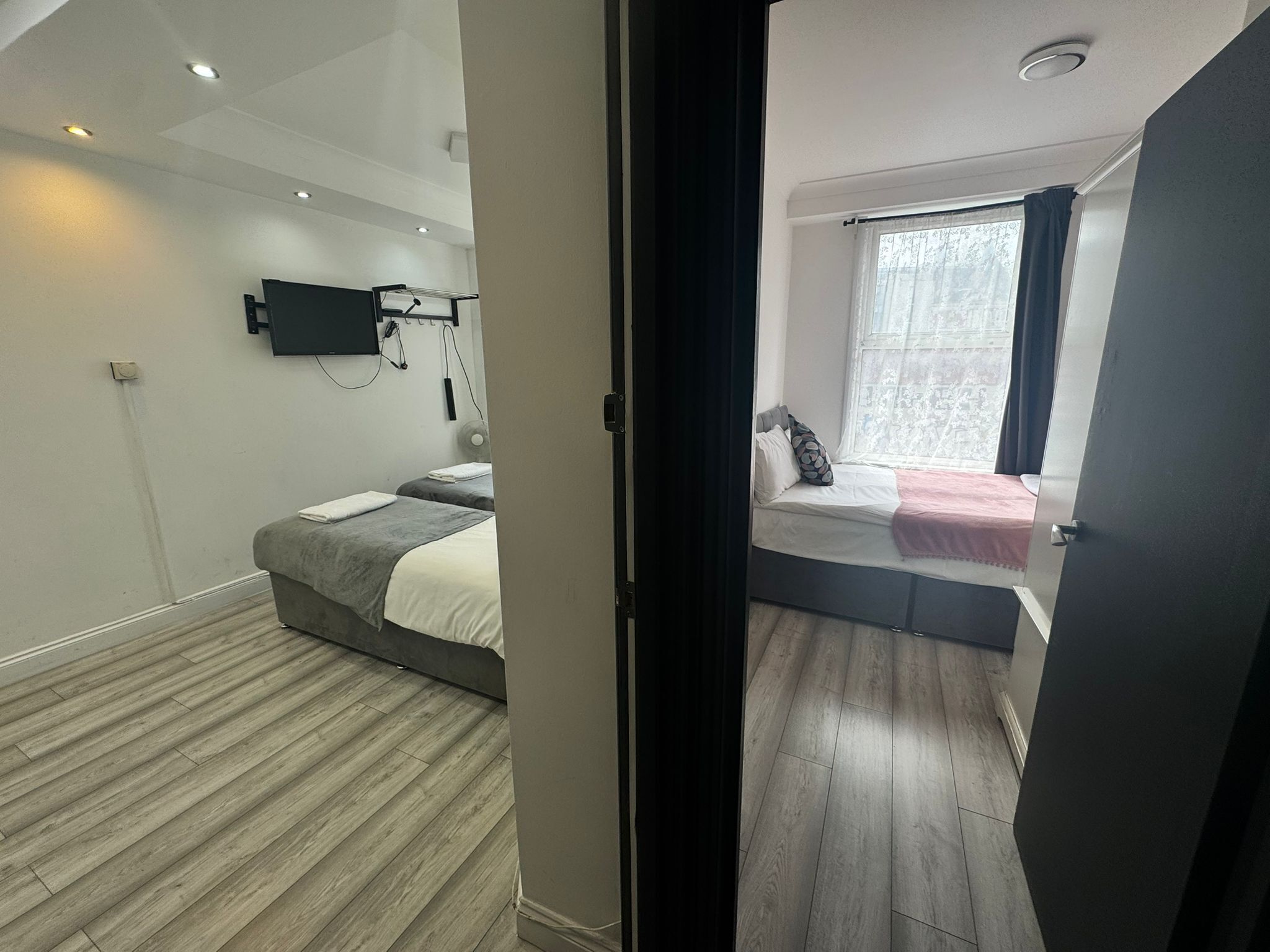 Quarto moderno com duas camas, uma TV fixada na parede e uma janela com cortinas.