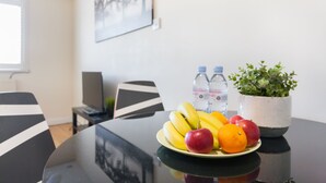 Une table à manger avec une assiette de fruits, deux bouteilles d’eau et une plante en pot.