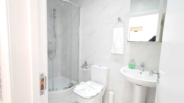 A modern bathroom with a glass-enclosed shower, a toilet, and a sink with a mirror above it.