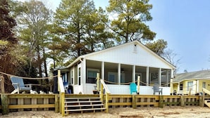 Une maison de plage avec un porche, une terrasse en bois et une plage de sable.