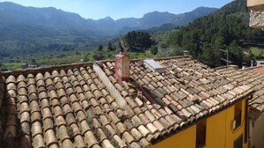 A yellow building with a tiled roof overlooking a valley with mountains in the background.