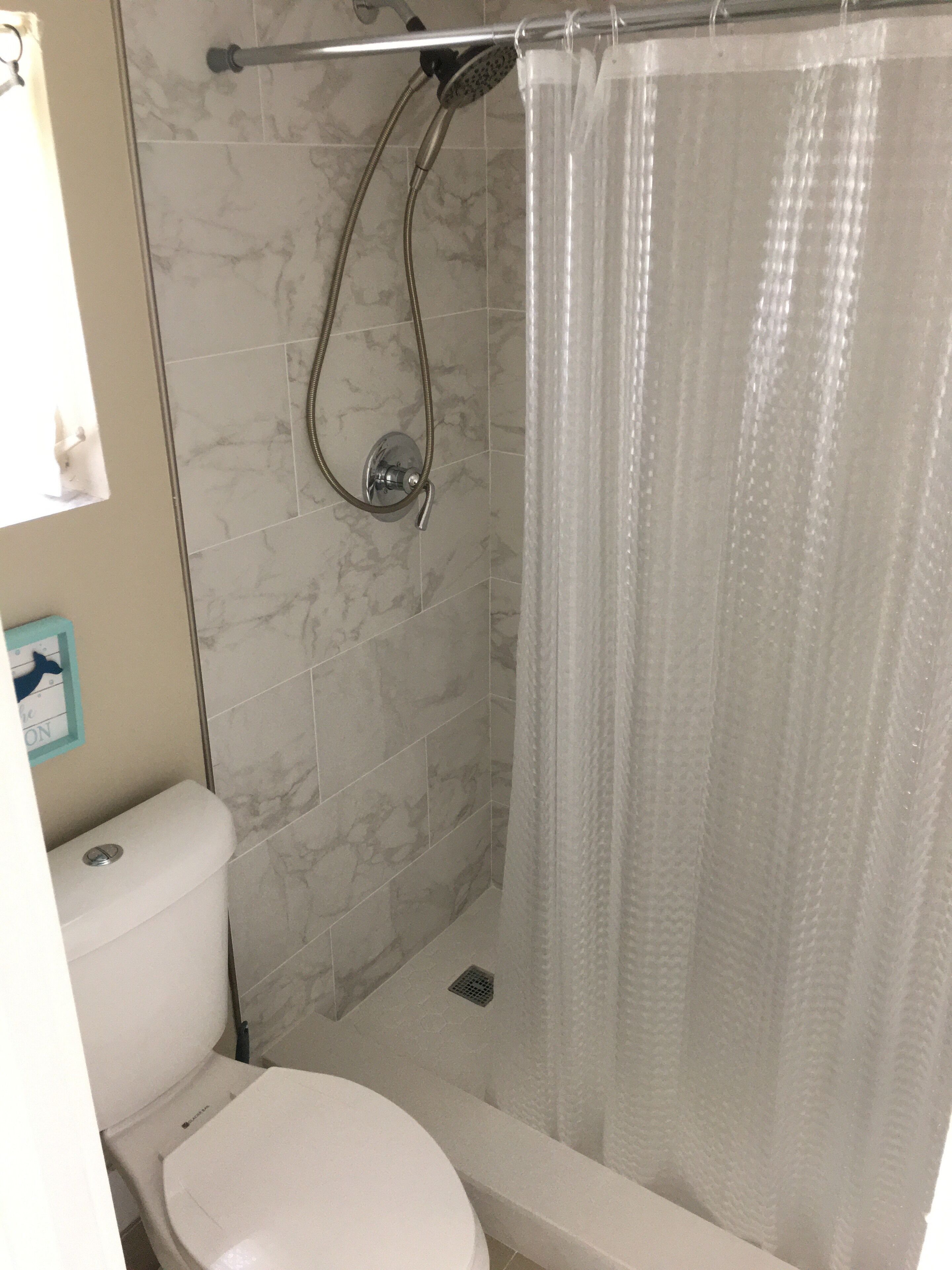 A bathroom with a toilet, a shower with a glass door, and a marble-tiled wall.