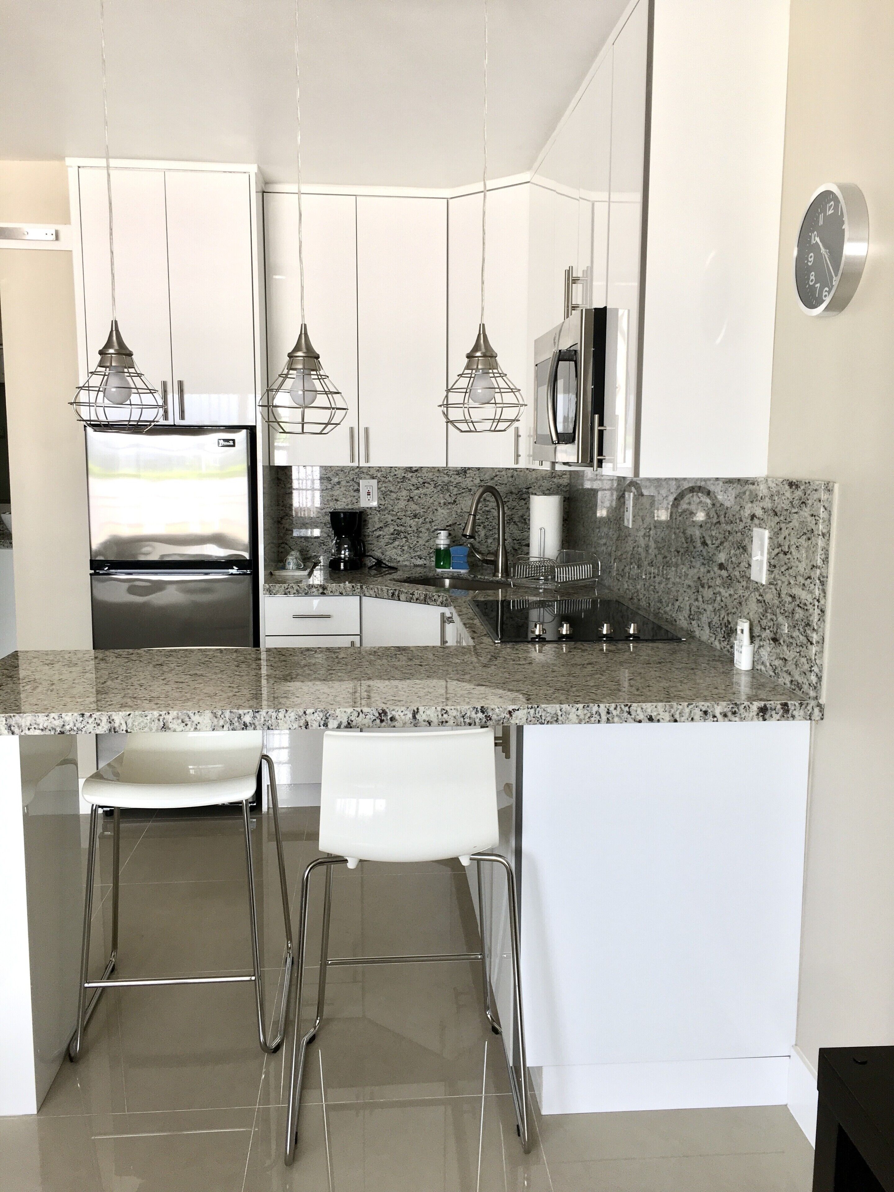 A modern kitchen with white cabinetry, granite countertops, stainless steel appliances, and pendant lighting.