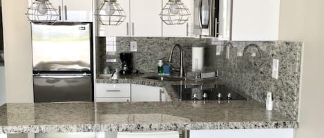 A modern kitchen with white cabinetry, granite countertops, stainless steel appliances, and pendant lighting.