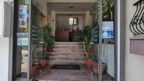 Entrada de hotel con una escalera de mármol, plantas en macetas y un felpudo de bienvenida.