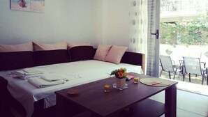 Un dormitorio con cama, una mesa con un florero y vasos, y vista al exterior.