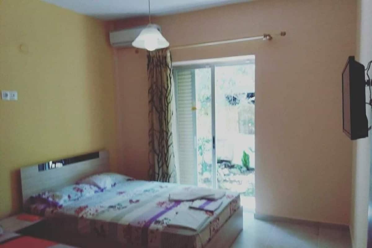 Ein Schlafzimmer mit einem Bett, einem Deckenventilator, einem Fenster mit Vorhängen und einem an der Wand montierten Fernseher.