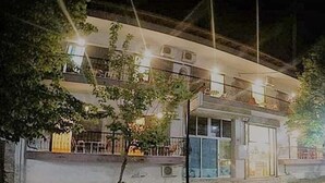 Un edificio de dos pisos con techo plano, un balcón en el nivel superior y un camino pavimentado en la parte frontal.