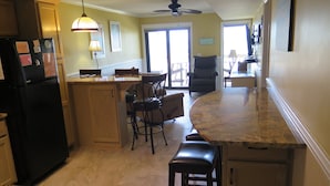 Une cuisine équipée d’un réfrigérateur, d’un coin repas avec des chaises, d’un tabouret de bar et d’un ventilateur de plafond.