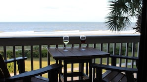 Une terrasse en bois avec deux chaises et une table, donnant sur une plage avec l’océan en arrière-plan.
