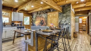 A rustic kitchen with wooden beams, a stone wall mural, and a bar area with stools.