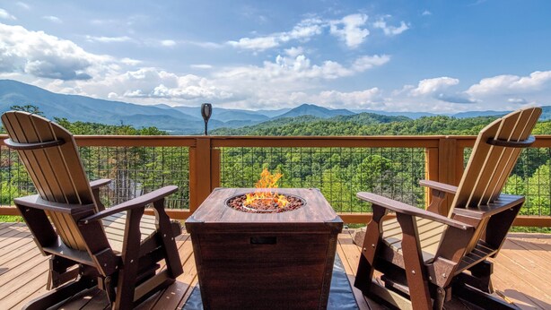 A deck with Adirondack chairs and a fire pit, overlooking a mountainous landscape.